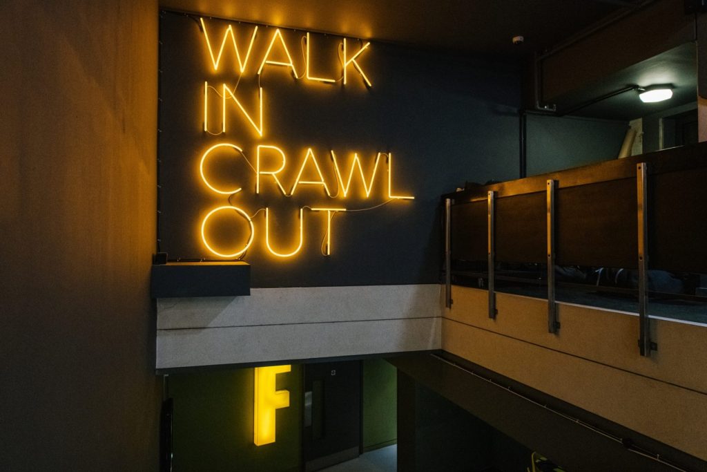 Neon sign reading 'Walk in, Crawl out' at Gymbox in Covent Garden