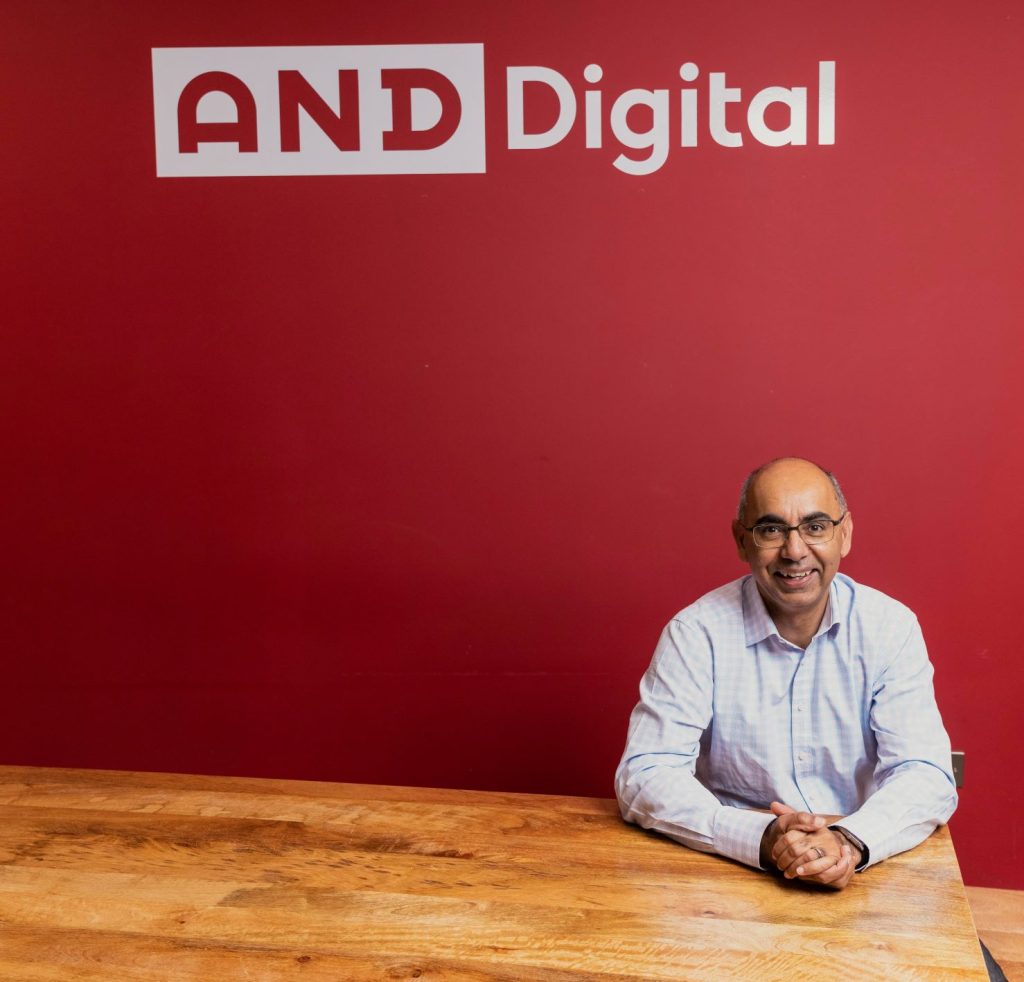 Paramjit Uppal, founder of AND Digital, sat in front of a branded backdrop