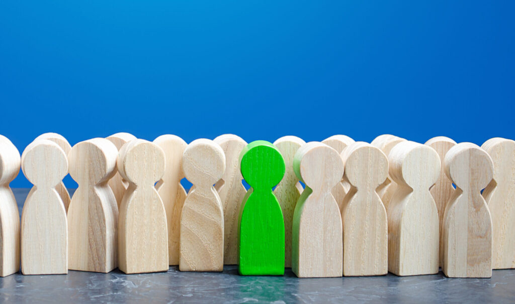 Group of wooden figures with one stood out in green - showing candidate selection