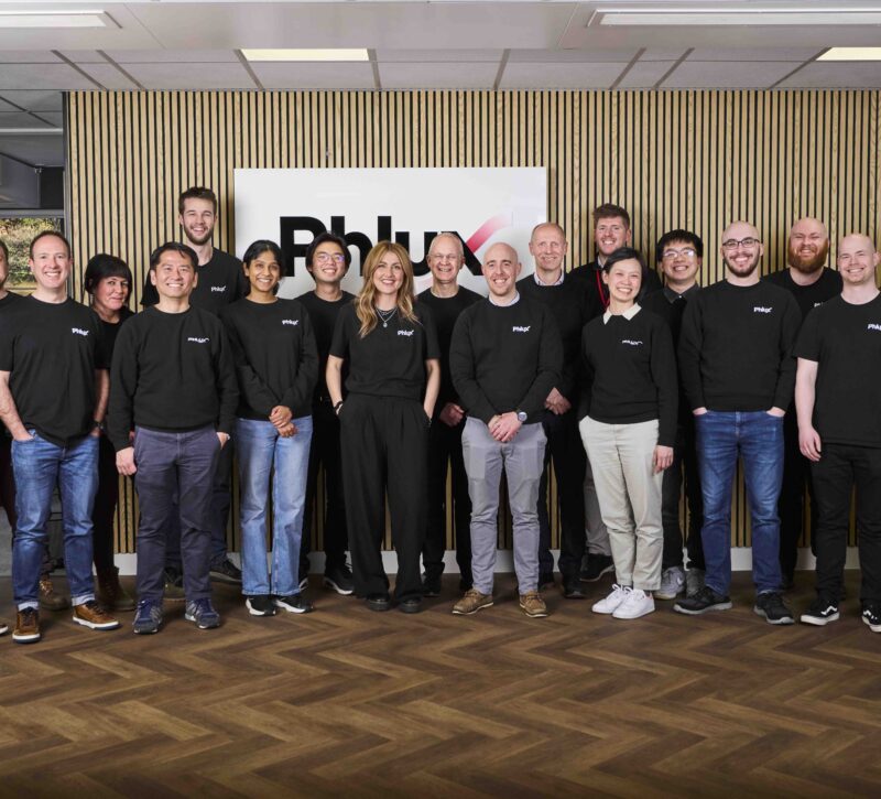 Phlux Technology team photo, in front of logo wall